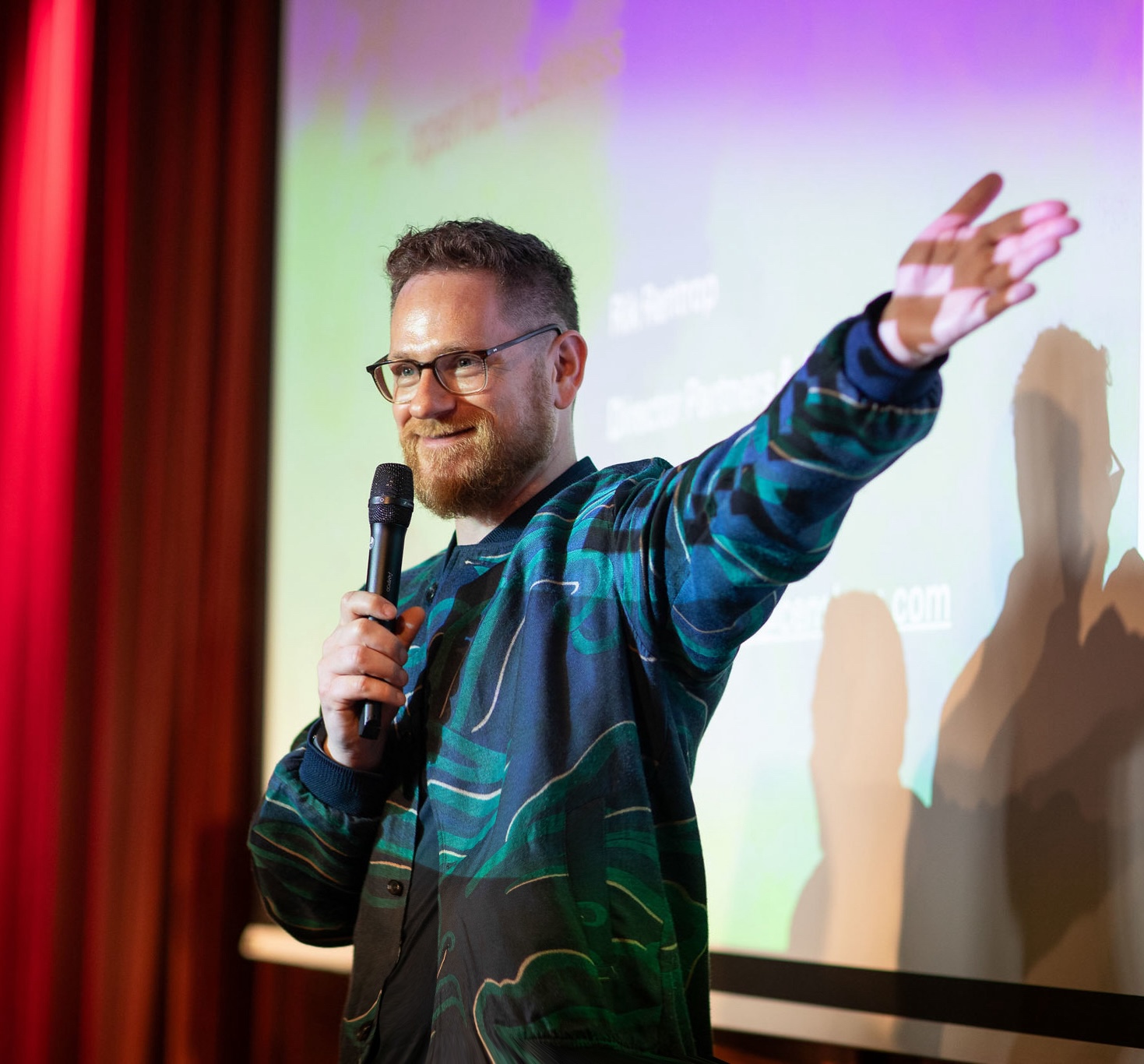 dagvoorzitter oliver in actie op podium met microfoon en wijzende arm